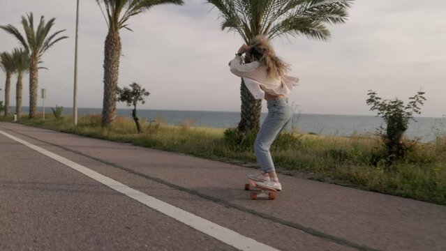 Teenage girl on skateboard skating on beach street with palm trees