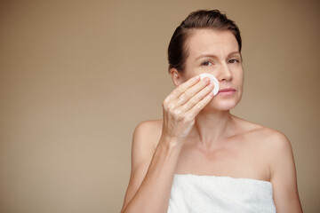 Mature woman wiping off make-up with cotton pad soaked in micelar water