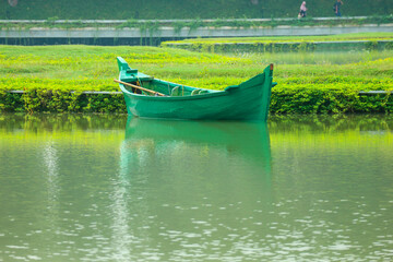 A green boat without passengers was parked on the edge of the lake.