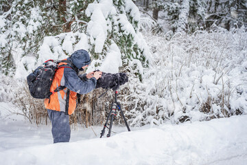 Professional Cameraman with camera shooting natural footage in snow forest. Behind scene