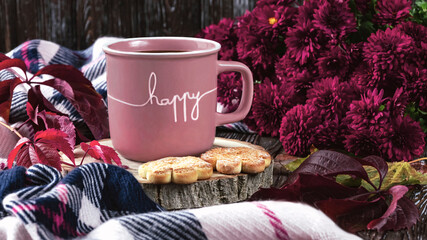 A pink cup of coffee, burgundy asters, autumn grape leaves, cookies and a scarf. Happy autumn mood. Autumn composition on a dark background.