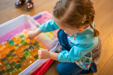 Little girl playing with sensory water beads, hydrogel balls. Sensory development and experiences, themed activities with children, fine motor skills development