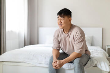 Happy asian man enjoying happy morning, sitting on bed
