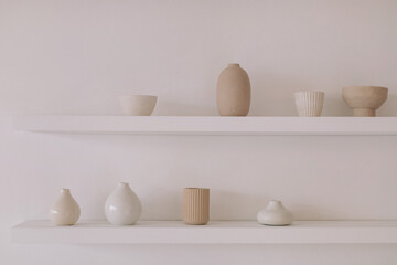 Fototapeta na wymiar Ceramic products of different shapes on a shelf on a white wall. Aesthetic home decor. Minimalistic background.