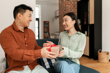 Loving asian man giving birthday gift to her lovely wife, having marriage anniversary celebration, exchanging gifts