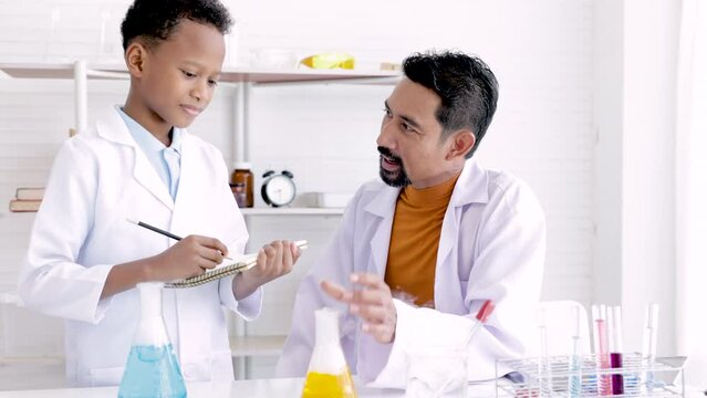 Teacher in white gown teaching cute african boy present the result experiment in science class at school, young science kid happy learning in chemistry class acting professional specialist.