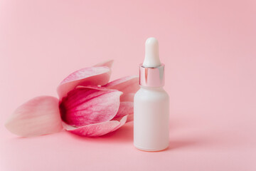 Cosmetic white serum bottle on pink background with magnolia flower. Mock up, copy space