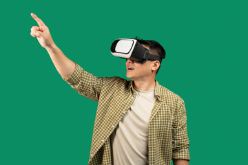 Asian man in casual and vr glasses touching empty space, pointing finger isolated on green background, studio shot