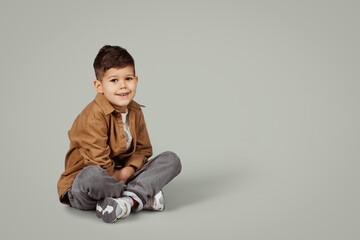 Cheerful caucasian 6 years old little boy in casual sit on floor with empty space