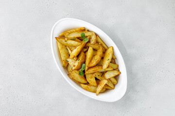 Baked potato wedges in white baking dish. Roasted potatoes with herbs and spices. Top view with...