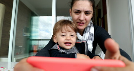 Happy baby toddler on mother lap watching content on cellphone. Child clapping hands feeling joy