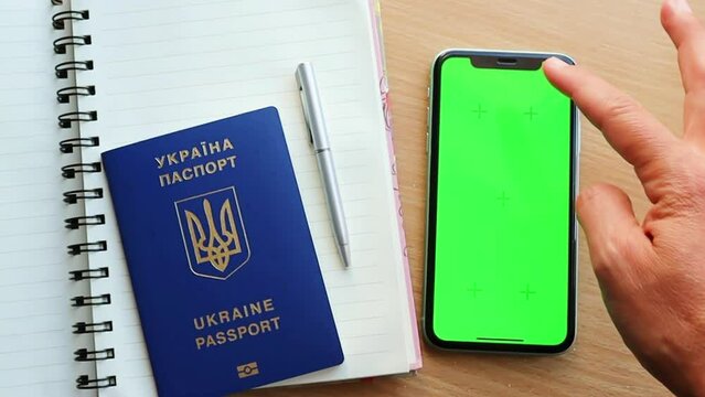 Woman's hand scrolling green screen browsing chroma key reading social media close up with Ukrainian passport and note book on the table
