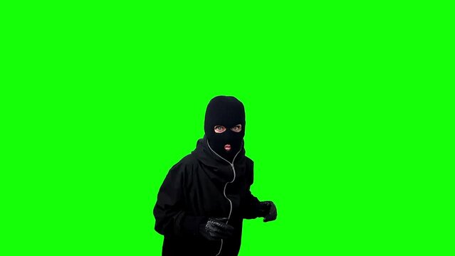 Catch concept. thief wearing a black balaclava and gloves raising his hands up isolated on a green background