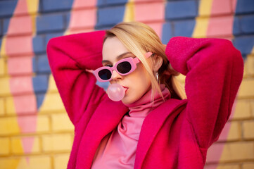 Fashionable confident blonde woman wearing trendy pink sunglasses, fuchsia color coat, turtleneck,...