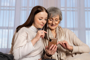 A young girl is explaining to an elderly woman how to use a phone. The granddaughter is showing her phone to her grandmother. a family pastime, helping and respecting the elderly.
