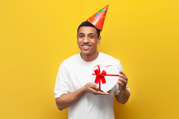 african american guy in festive hat celebrates his birthday and holds gift heart, man with box for...