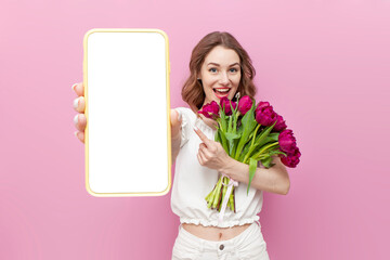 young attractive girl in white clothes holds bouquet of pink tulips and shows blank screen of...