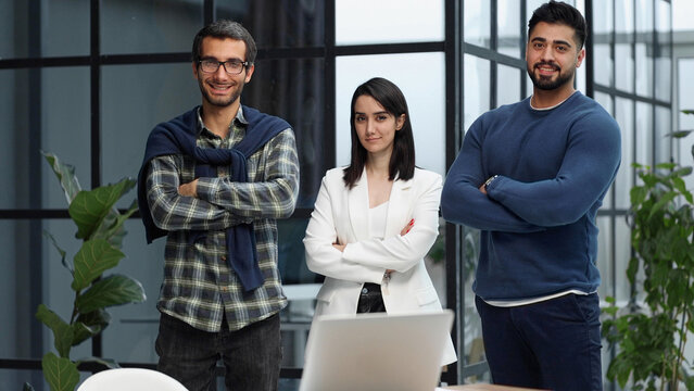 three colleagues stand in the lobby of a modern office with their arms crossed
