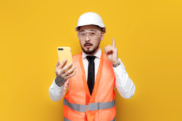 asian foreman in uniform holding smartphone and pointing idea with his finger on yellow isolated background