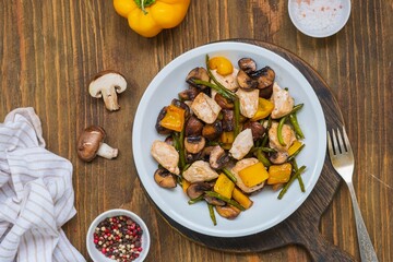 Chicken stew with mushrooms, sweet peppers and garlic arrows in a gray plate on a wooden background.