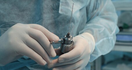 The surgeon changes the nozzle on a surgical drill during an operation on a broken bone. The...