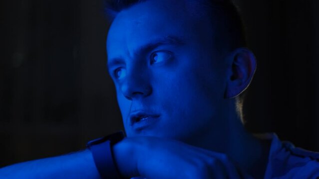 Young man recording voice message on smart watch at night in neon light, close-up