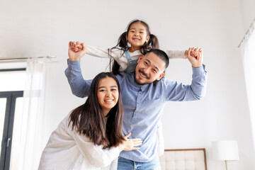 happy Asian family with a little daughter stand at home and rejoice, mom and dad hold the child in...