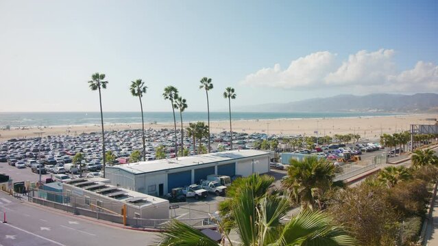 Handheld Shot Of Parking Lot near Famous Amusement Park On Pier. Beach Santa Monica, California. Blue bright Sky on sunny day. Cars on parking zone. Palms and threes. High quality 4k footage