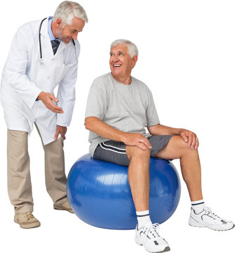 Fototapeta Male therapist looking at senior man sit on exercise ball