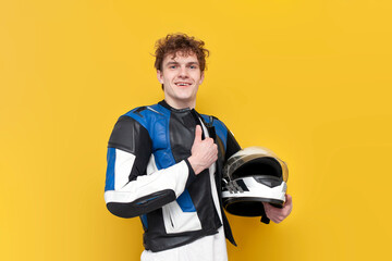 young guy motorcyclist in leather jacket holds helmet and smiles on yellow isolated background