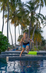 Little boy jumping from the side into the pool at sunset