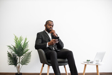 African american man looking aside with pensive facial expression while using modern smartphone at...