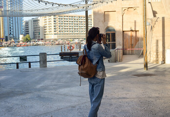 A young woman traveler with a backpack on her back walks and photographs the old narrow streets of Dubai Deira and Creek. Travel and sightseeing concept.