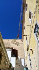 Fototapeta na wymiar Behind the old walls of the house you can see a construction crane against the blue sky in Lisbon
