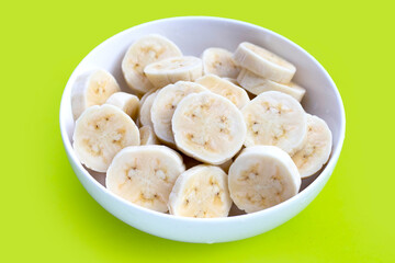 Banana slices in bowl on green background.