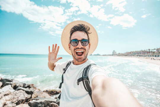 Handsome young man taking selfie at beach summer vacation - Smiling guy having fun walking outside - Summertime holidays and technology concept - Powered by Adobe