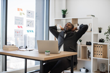 Fatigued and sleepy african man in suit yawning in chair while overwhelmed with work at office....