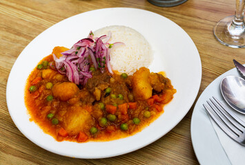 Plate of tasty Peruvian dish - spicy veal served with gravy, rice and onion