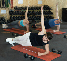 Concentrated young guy holding side plank pose to strengthen body muscles during intense group training in gym. Effective core exercises. Active lifestyle concept..