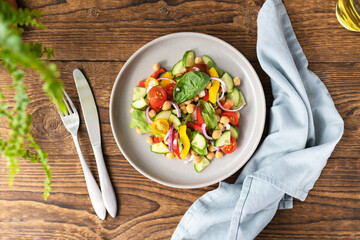 Vegetarian vegetable salad with chickpeas, tomatoes, red onions, cucumbers and lettuce. Vegetarian food rich in protein and fiber. Vegetable salad on wooden table top view