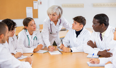 Elderly female doctor conducts training for interns of different ages at round table in auditorium...