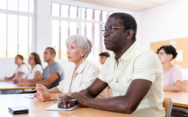 Concentrated african american man listening attentively and taking notes of lecture during adult education class