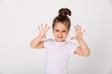 Cute little girl in white T-shirt washes her hair in the bathroom and shows soap palms foam