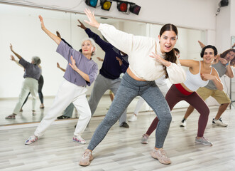 Happy young woman practising modern dance moves with other people in dance studio
