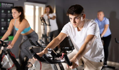 Fototapeta na wymiar Portrait of concentrated young guy doing cardio training, cycling on stationary bike in gym. Sport and fitness concept