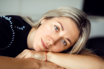 Beautiful blonde woman of 40 years has put her head on her folded hands and is looking intently at camera. Portrait. 