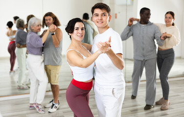 Young smiling guy learning to dance waltz paired with expressive positive Hispanic girl in dancing...