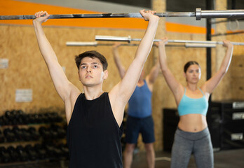 Young male bodybuilder performing strength and endurance exercises during group barbell lifting in CrossFit class