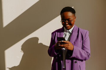 African american businesswoman using smartphone while standing over a white wall in an office