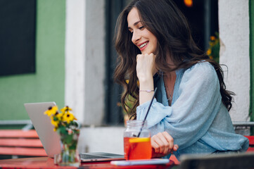 Beautiful woman sitting in a street cafe and using laptop